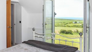 Quarto com uma cama, vista para uma paisagem verde e uma porta.