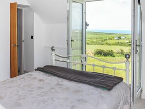 Ein Schlafzimmer mit einem Bett, Blick auf eine grüne Landschaft und einer Tür.