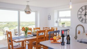 Uma cozinha moderna com cadeiras de madeira, uma mesa de jantar, uma janela ampla e vista para o campo.
