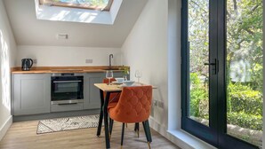 Una cocina moderna con tragaluces, una zona de comedor con mesa y sillas, y un amplio ventanal con vistas al verdor.