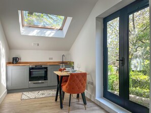 A modern kitchen with a skylight, a dining area with a table and chairs, and a large window with a view of greenery. - 1 bedroom accommodation in Meltham, near Holmfirth (Meltham, near Holmfirth)