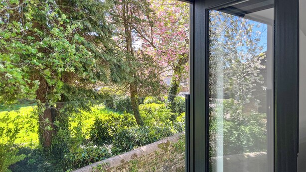 Vista a través de una ventana con un muro de piedra y follaje.