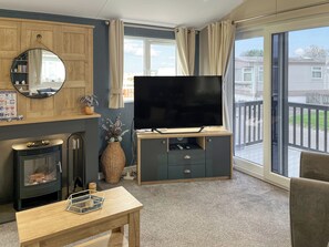 Una sala de estar con chimenea, un televisor de pantalla plana, una mesa de centro de madera y un ventanal con vistas al exterior.