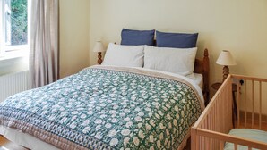 Una camera da letto con un letto, una culla, una finestra con tende e una lampada.
