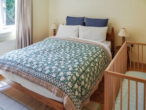 A bedroom with a bed, a crib, a window with curtains, and a lamp.
