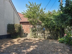 A gravel driveway leading to a wooden gate with a brick building in the background.