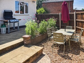 A patio with a table and chairs, a barbecue grill, and a garden bed with flowers.