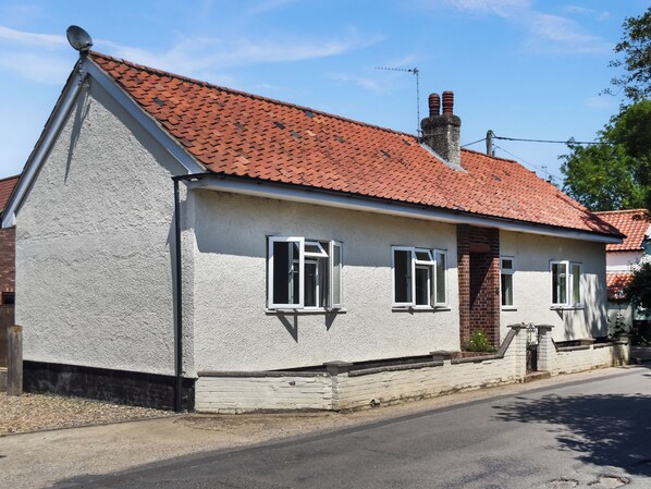A single-story house with a red-tiled roof, white exterior walls, and a brick foundation.