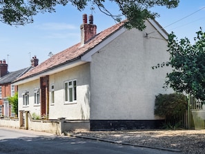 A single-story house with a pitched roof, a brick chimney, and a white exterior wall.