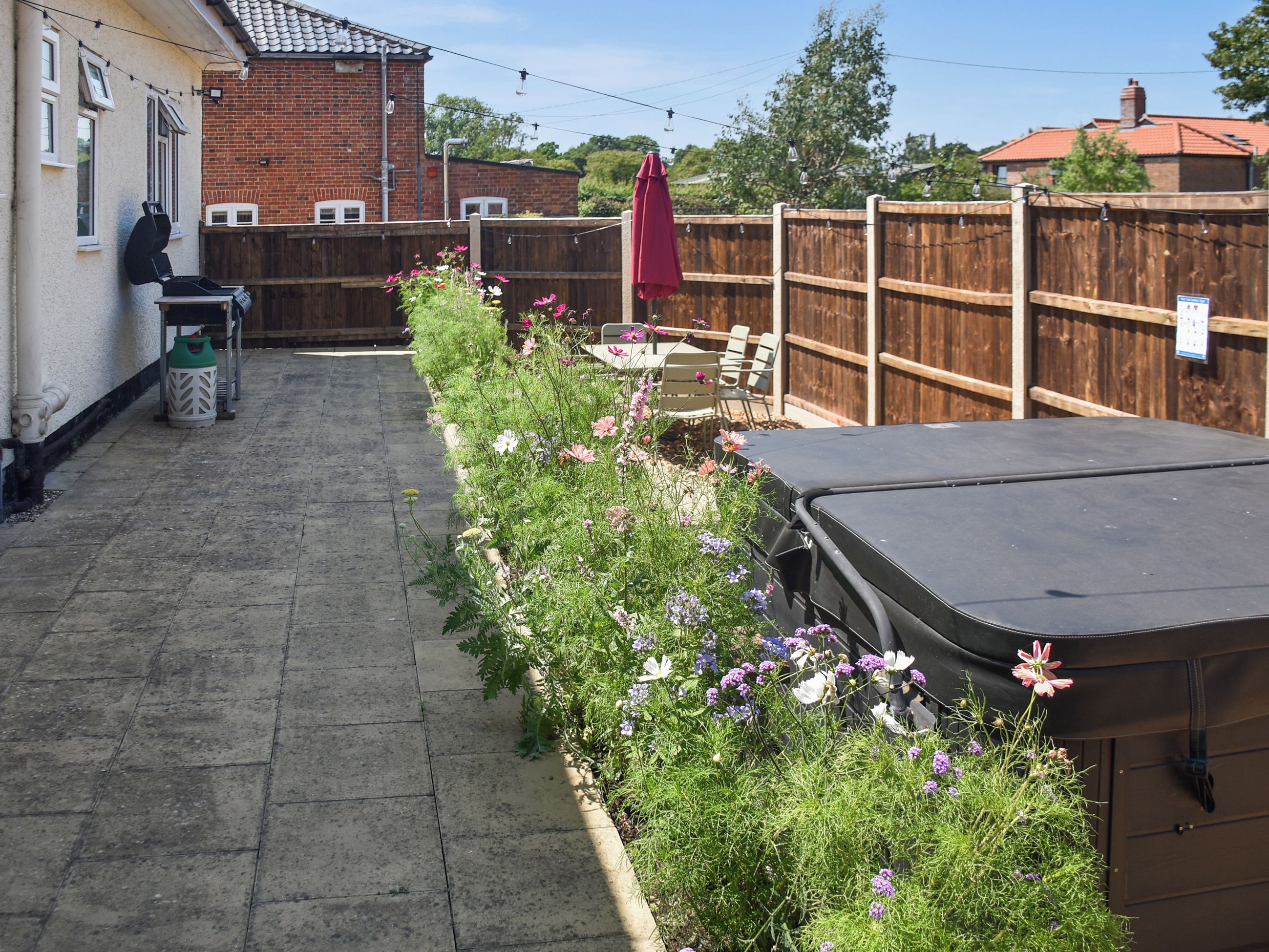 A backyard with a barbecue grill, a wooden fence, and a variety of flowering plants.