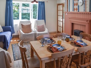 A dining area with a wooden table set for four, surrounded by chairs, with a view of greenery outside.