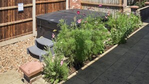 Un giardino sul retro con un barbecue, una recinzione in legno e aiuole con diverse piante e fiori.