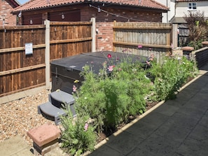 A backyard with a barbecue grill, a wooden fence, and a garden with various plants and flowers.