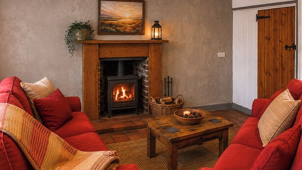 Uma sala de estar aconchegante com lareira, sofás vermelhos, mesa de centro de madeira e um quadro sobre a lareira.