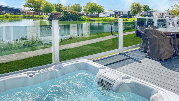 A hot tub on a wooden deck with a view of a lake and a row of houses in the background. - Serenity at Lakeside - UK51947 (Patrington Haven)