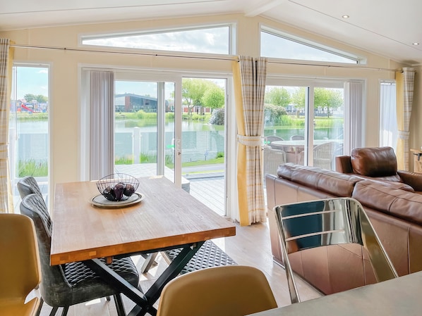 Amplia habitación con mesa de comedor, sillas, sofá y ventanas grandes con vistas a una masa de agua y vegetación.