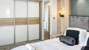 A hotel room with a bed, a nightstand, a wall-mounted light, and a sliding door. - Serenity at Lakeside - UK51947 (Patrington Haven)