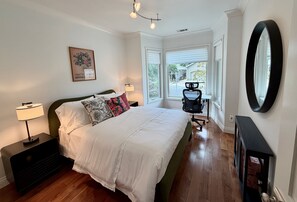 Une chambre à coucher avec un lit, une table de chevet, une lampe, une fenêtre et un grand miroir.