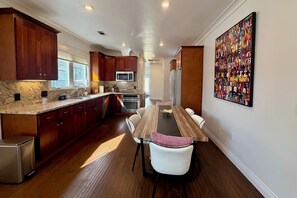 Une cuisine avec des meubles en bois, un plan de travail en marbre, une table à manger avec des chaises, un réfrigérateur et un tableau abstrait aux couleurs vives accroché au mur.