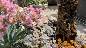 Un jardín con cerca de madera, una formación rocosa y varias plantas.