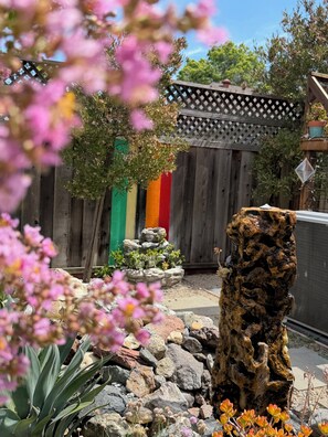 Un giardino con una recinzione in legno, una formazione rocciosa e diverse piante.