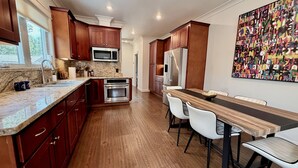 Una cocina moderna con armarios de madera, electrodomésticos de acero inoxidable y una zona de comedor con una mesa de madera grande y sillas blancas.