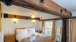Un dormitorio con una cama de madera, mesitas de noche, una lámpara de noche, una ventana con cortinas y una viga de techo de madera.