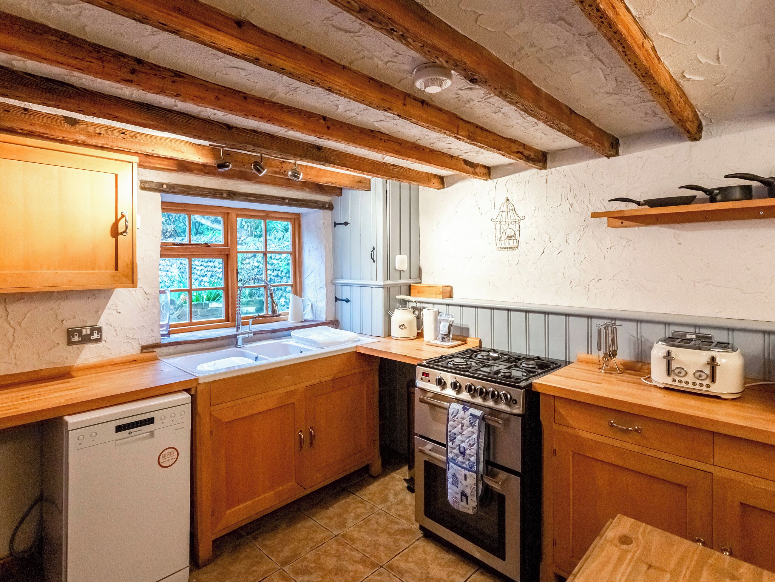 A kitchen with wooden cabinets, a stove, a sink, and a window with a view of greenery.