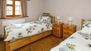 A bedroom with a wooden bed, two bedside tables, a window with curtains, and a radiator. - Bay Cottage - UK51915 (Broadstairs)
