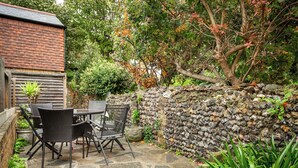 A patio with stone flooring, a table, chairs, and a stone wall. - Bay Cottage - UK51915 (Broadstairs)