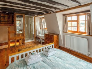 A bedroom with a wooden floor, a bed with a blue and white patterned bedspread, a wooden dresser, a chair, a window with curtains, and a radiator. - Bay Cottage - UK51915 (Broadstairs)