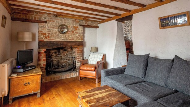 A cozy living room with a fireplace, a sofa, a wooden coffee table, and a television on a side table. - Bay Cottage - UK51915 (Broadstairs)