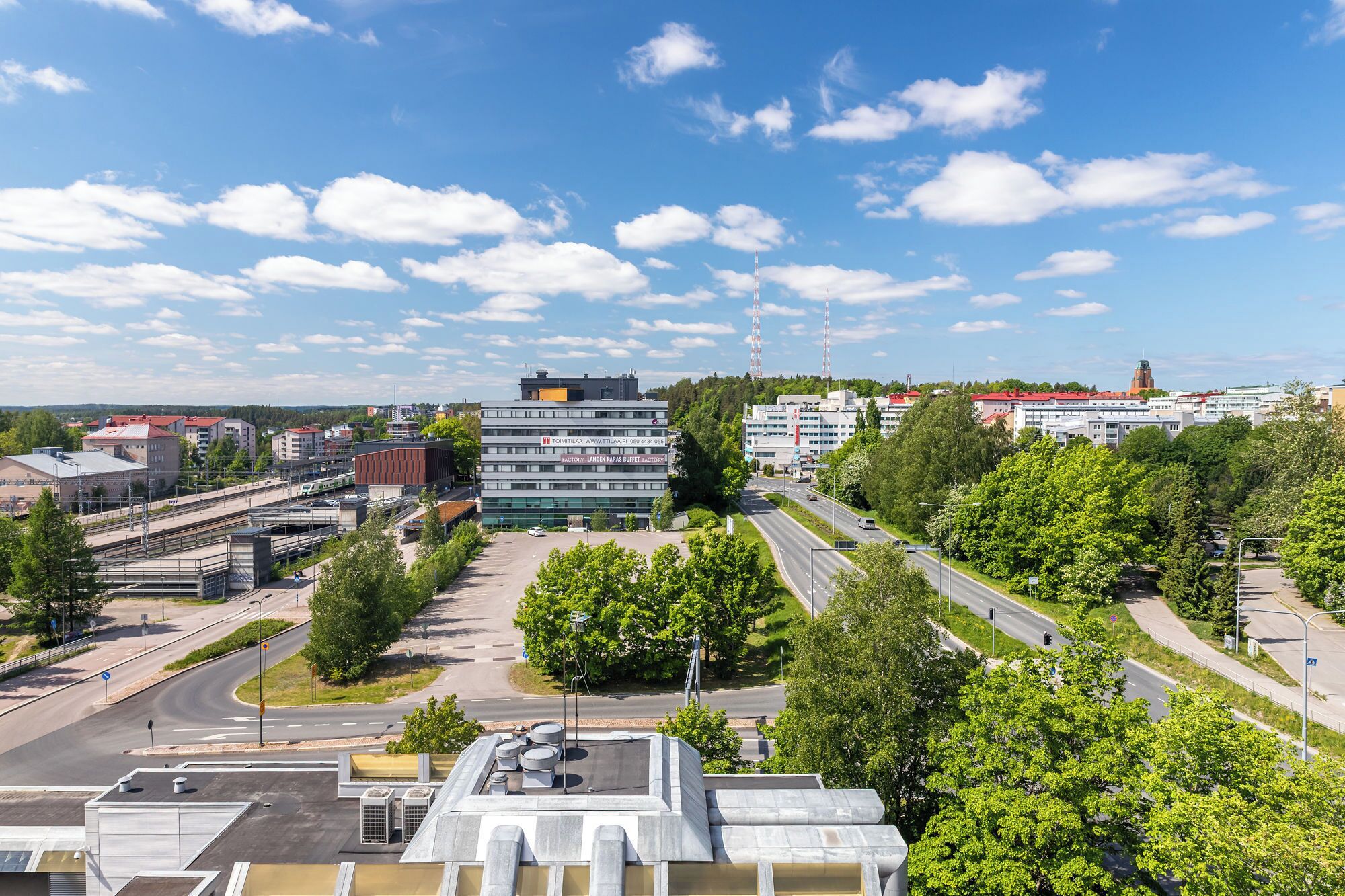 A modern building with a flat roof, surrounded by greenery and a clear sky.