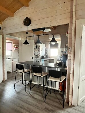 Une cuisine dotée d’un îlot central, de tabourets de bar, de luminaires suspendus et d’une horloge bien visible.