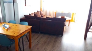 Et spiseområde med et træbord og blå stole, en brun sofa og et lille rundt bord med en skål.