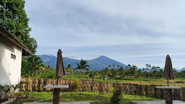 A courtyard with two stone tables, a bamboo fence, and a view of a mountain. - Botanika Estate (Tetebatu)