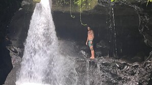 A man standing on a rock with a waterfall in a cave. - Botanika Estate (Tetebatu)