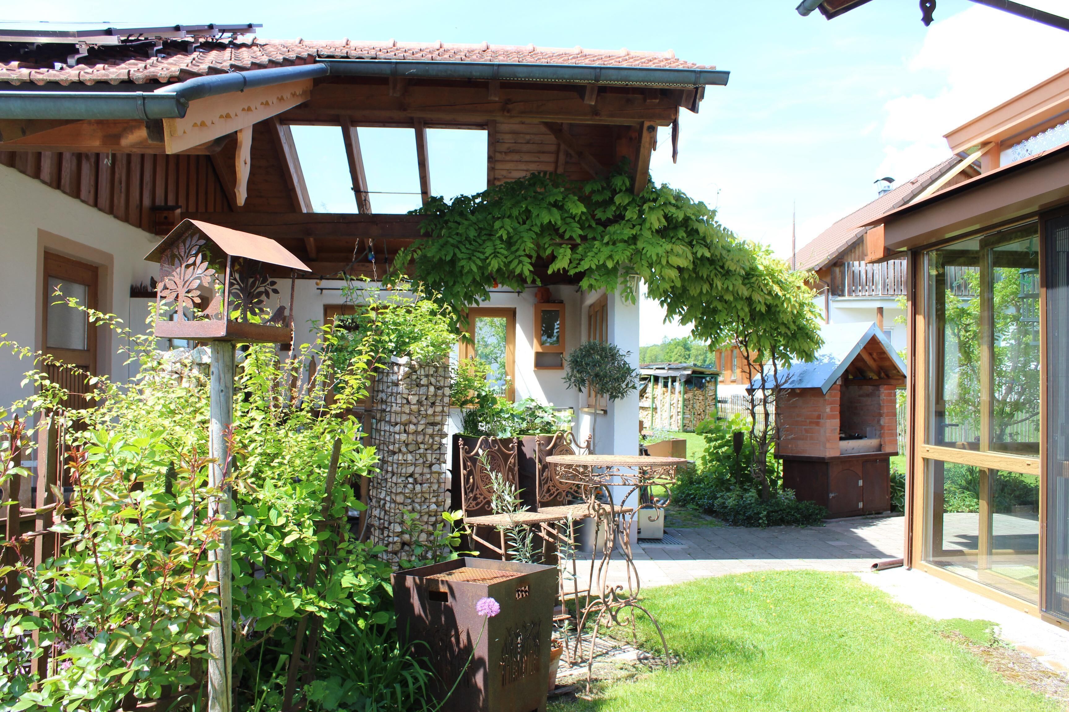 Ein rustikaler Außenbereich mit einer Holzpergola, einer Steinmauer und einem Backofen aus Ziegeln.