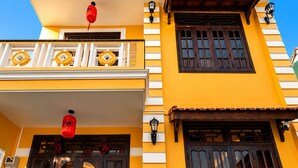 A two-story building with a yellow facade, dark wooden doors, and a balcony with railings. - Bao An Home (Hội An)