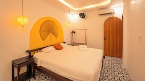A hotel room with a bed, bedside table, wall-mounted lamp, and a door. - Bao An Home (Hội An)
