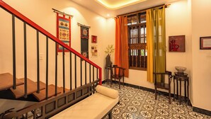 A staircase with a red railing, a bench, patterned floor tiles, a window with orange curtains, and a wall-mounted vase. - Bao An Home (Hội An)