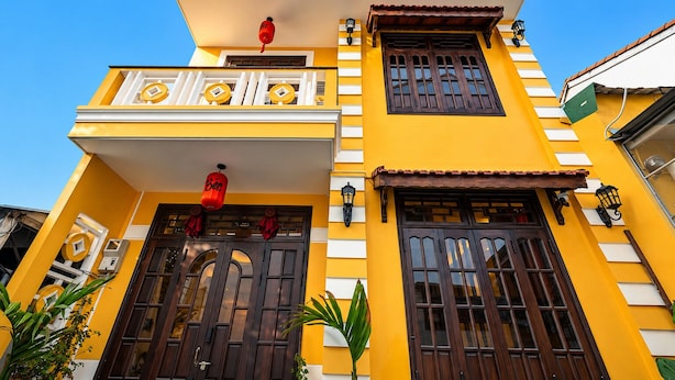A two-story building with a yellow facade, dark wooden doors, and a balcony with railings. - Bao An Home (Hội An)