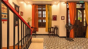 A room with patterned flooring, a wooden door, a staircase with a red handrail, and a fan. - Bao An Home (Hội An)