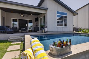 Ein Swimmingpool mit Liegebereich, einer überdachten Terrasse und einem Metallkübel mit Flaschen.