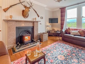 A living room with a fireplace, a sofa, a television, and a view of the outdoors. - The West Wing at Inverarnie Lodge (Inverness)