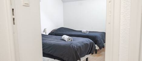 A room with two beds, white walls, and a wooden floor.