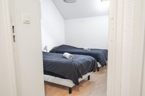 A room with two beds, white walls, and a wooden floor. - Duplex with balcony • Pool • Near Honfleur (La Rivière-Saint-Sauveur)
