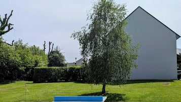 Eine Beton-Terrasse mit einer blau-weißen Bank, einem Baum und einem weißen Gebäude im Hintergrund.