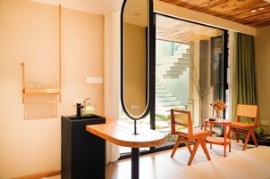 Ein modernes Zimmer mit einem großen Spiegel, einem kleinen Tisch, zwei Stühlen und Blick auf eine Treppe sowie Grünfläche draußen.