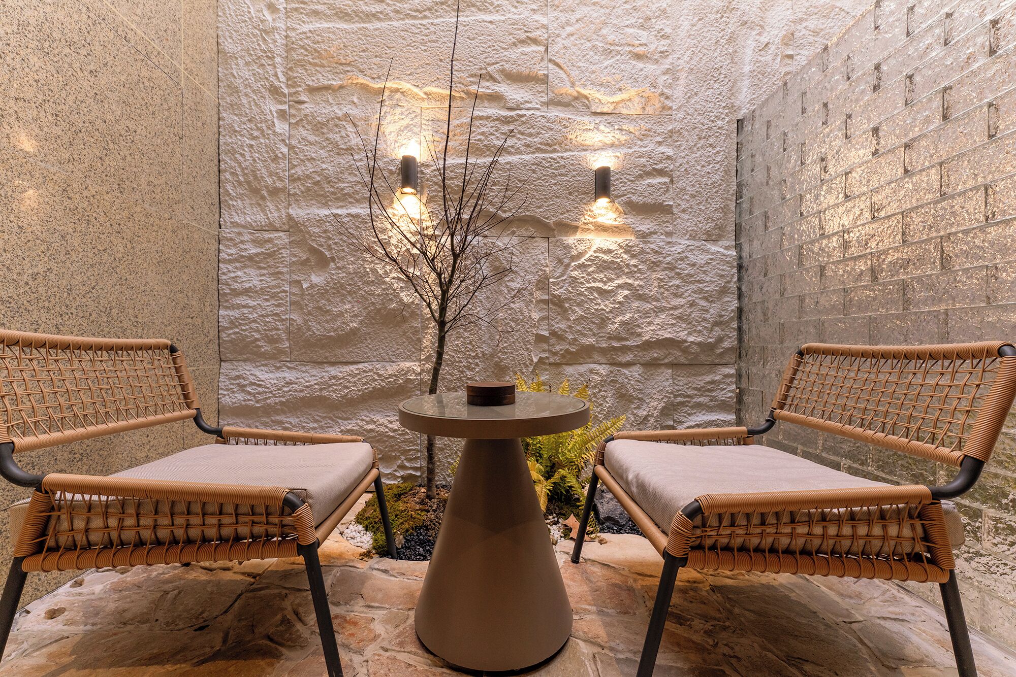 Un mur de pierres, avec deux chaises en osier et une table, chacune agrémentée d’une bougie.